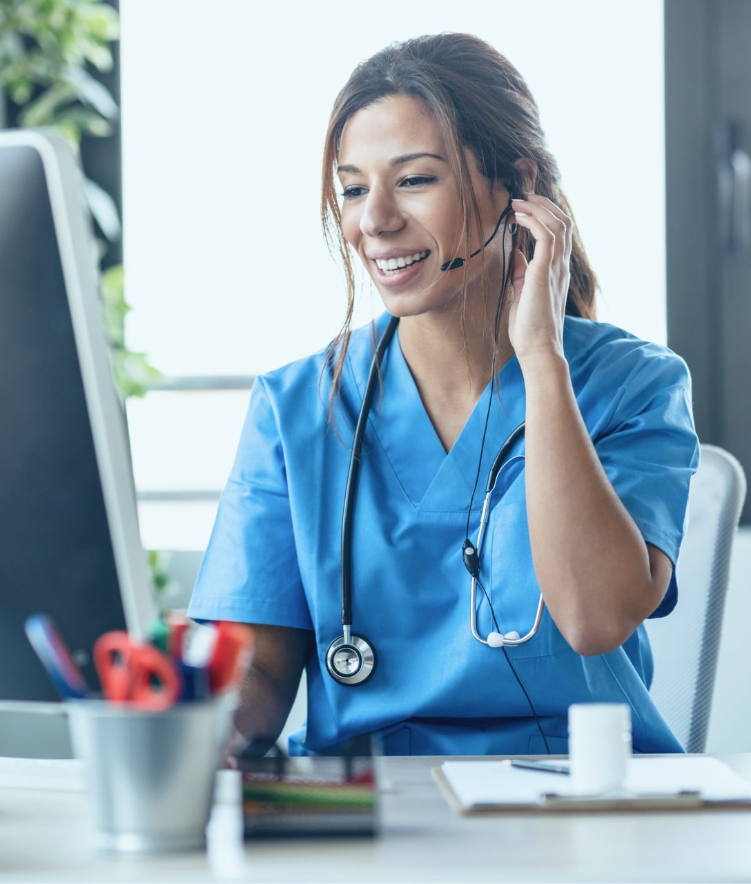 Female nurse with headset and stethoscope delivering patient engagement services at her desk.