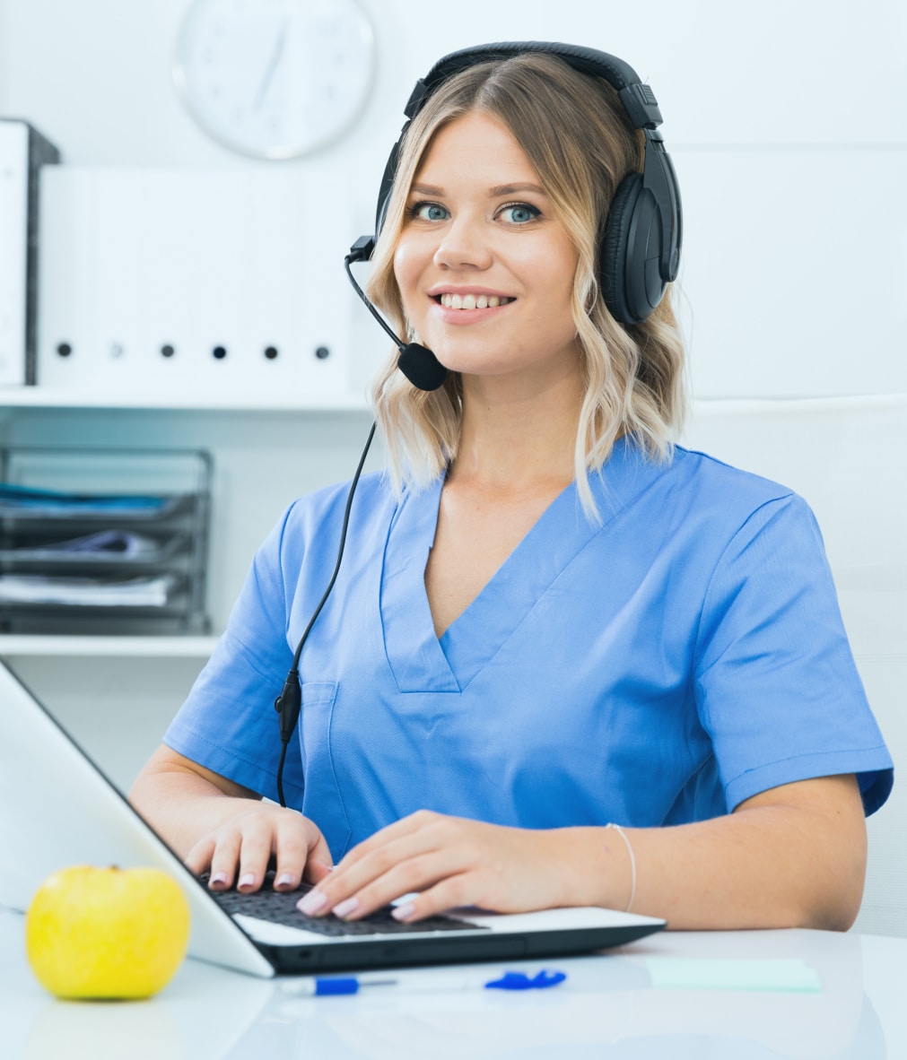 Nurse providing patient support programs while on a call with a headset, typing on her laptop.