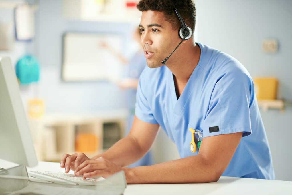 Male nurse delivering patient outreach and buy-and-bill support during a call while typing on a laptop.