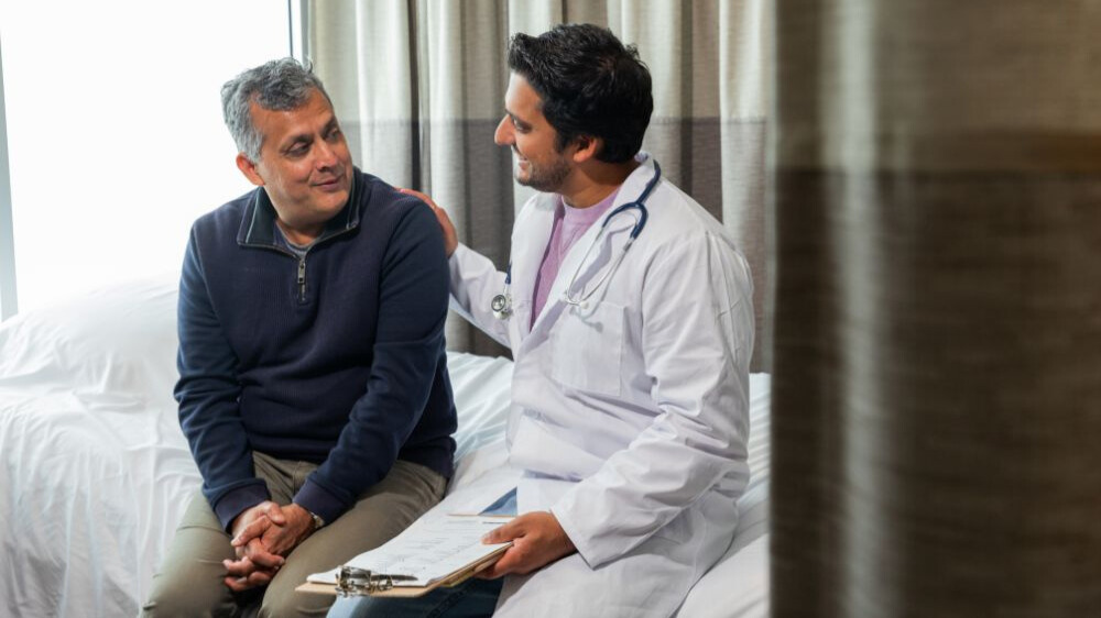 A Doctor explains patient retention strategies with a male patient in a hospital room.