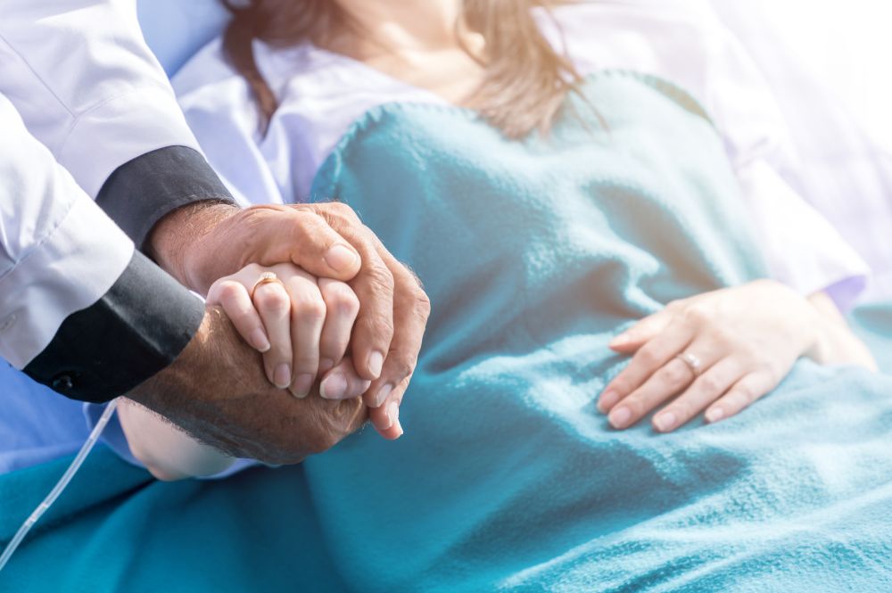 A Doctor holds a patient's hand in a time of need showcasing the patient support program and patient engagement.
