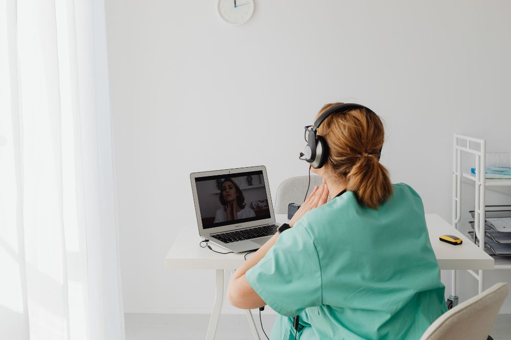 A nurse wearing a headset performs a clinical site follow-up with a patient over video chat