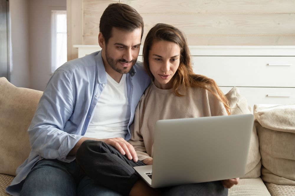A man and woman sit on a couch, focused on a laptop showcasing the Patient Support Program technology platform.