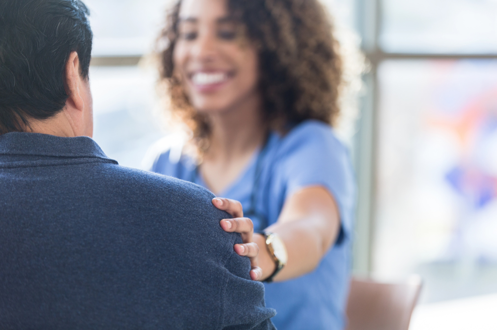A female nurse converses with a man about improving patient adherence in clinical trials.