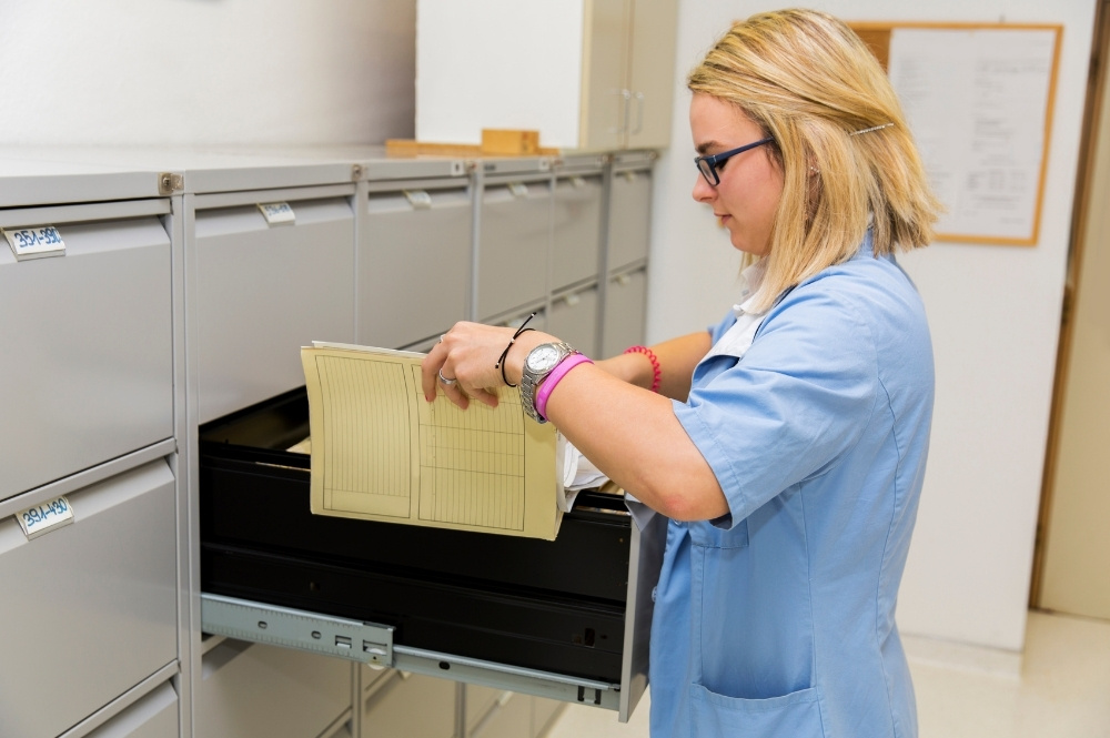 Healthcare professional retrieving a patient medical record from filing cabinets for clinical trial eligibility review