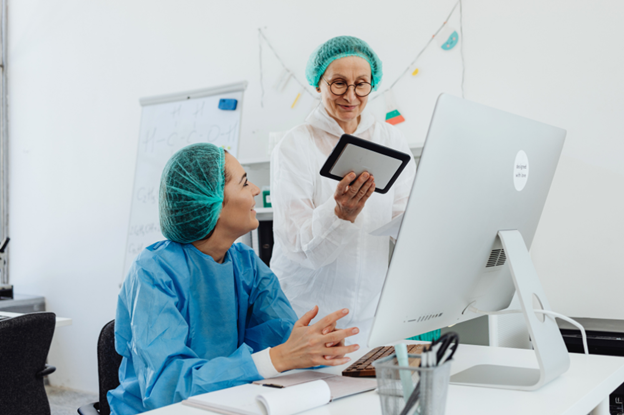 Two women in scrubs collaborating on a computer, focusing on clinical trial patient recruitment strategies.
