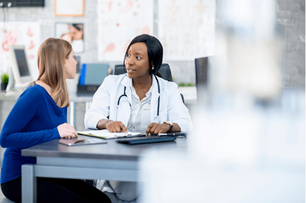 A woman discusses her health with a doctor in an office, highlighting patient adherence programs for better outcomes.