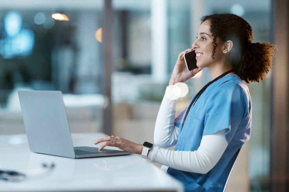 Nurse providing clinical trial site support by coordinating patient follow-up on the phone while using a laptop
